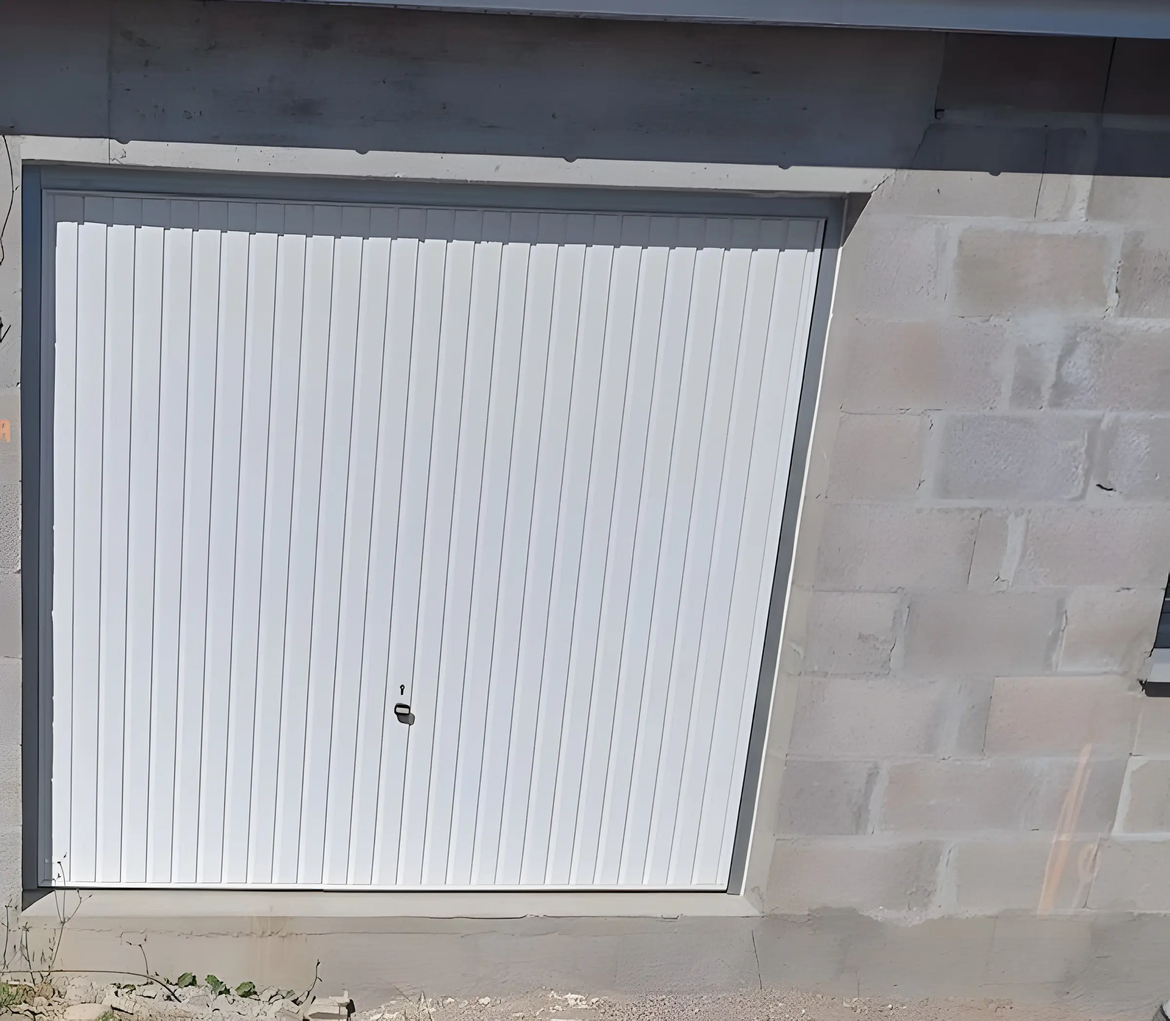 Porte de garage basculante blanche à rainures verticales dans un mur en parpaings, petite fenêtre anthracite à droite