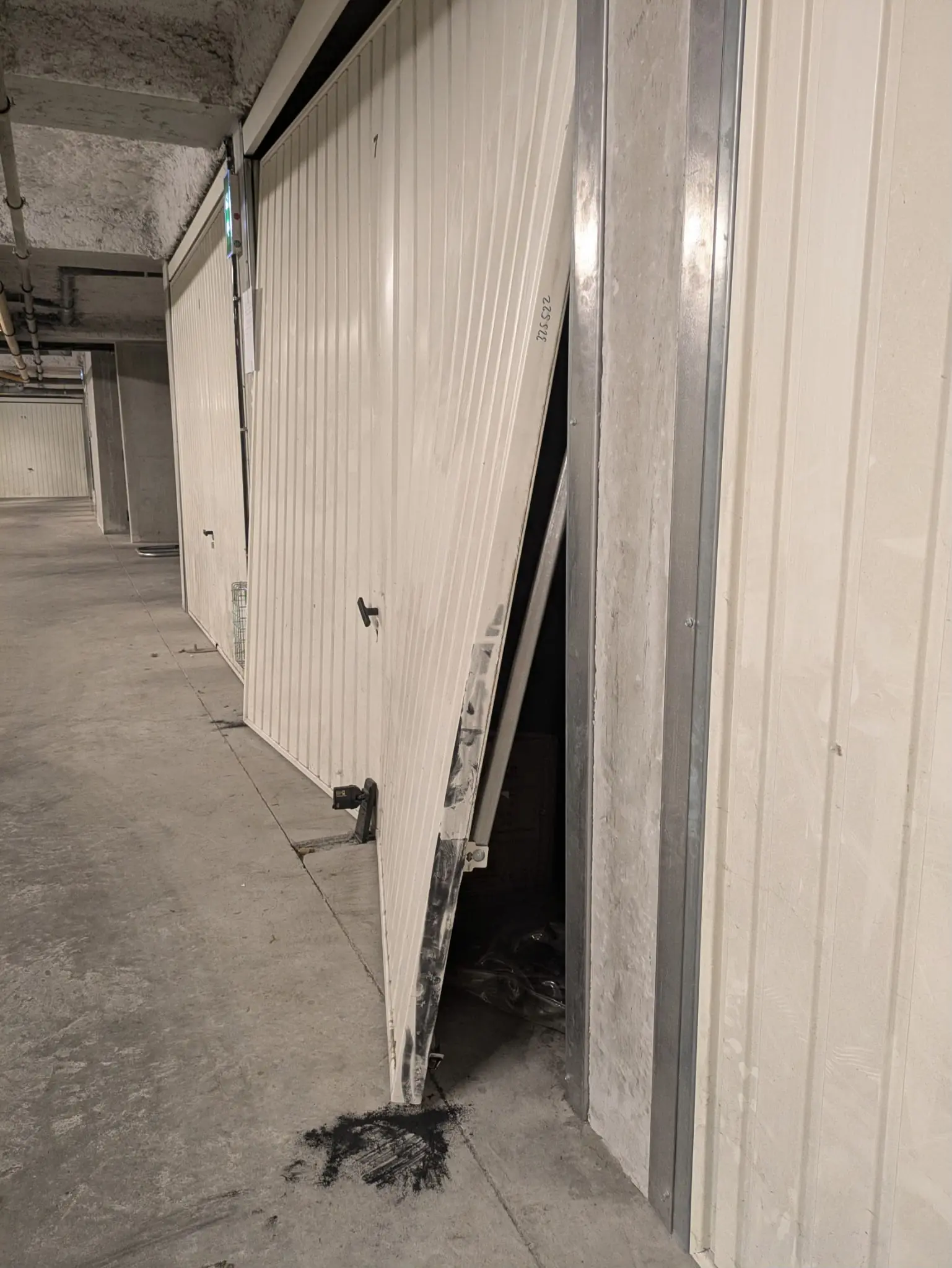 Porte de garage basculante blanche forcée, bas du tablier tordu et écarté du cadre, parking souterrain